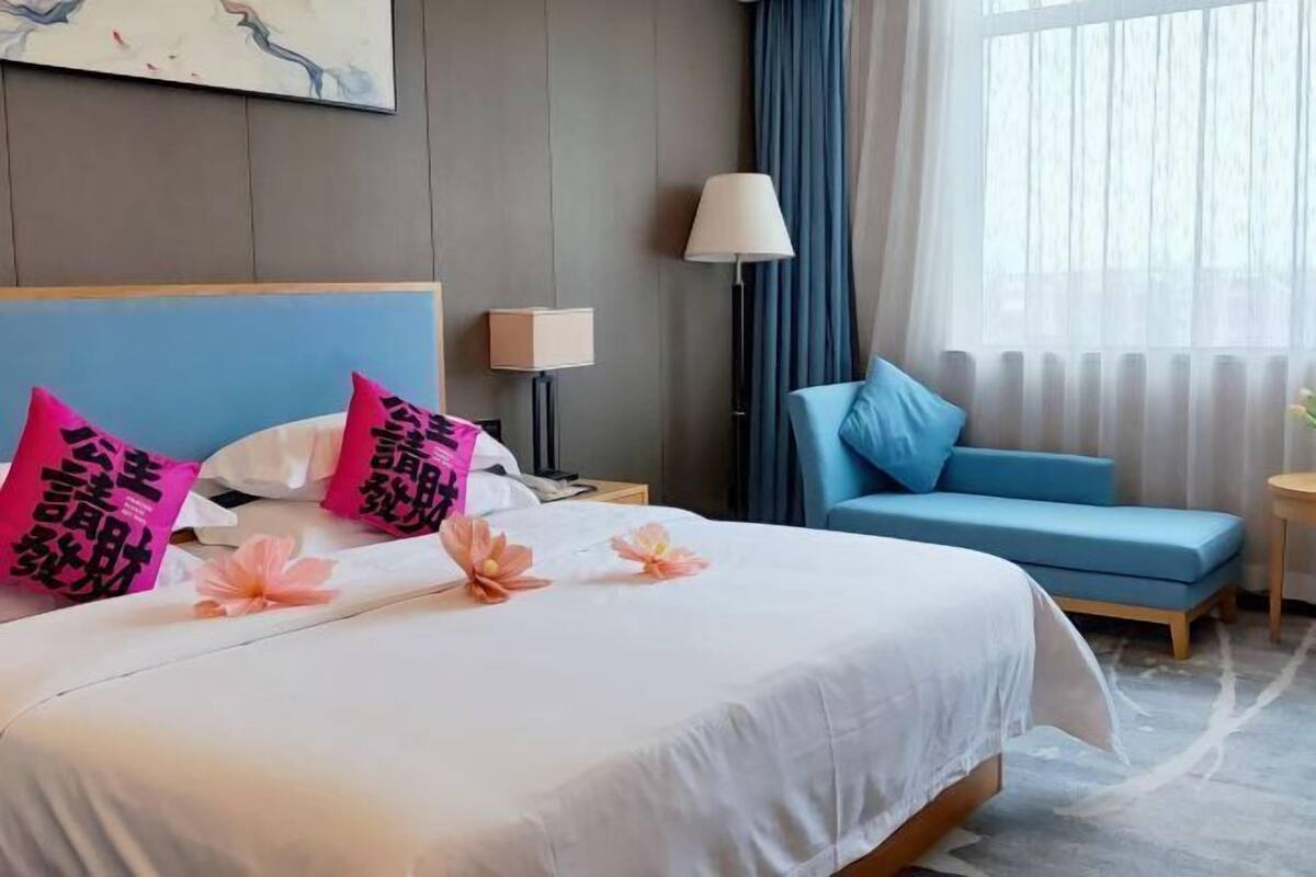 Une chambre d’hôtel avec un lit, un canapé bleu, une lampe et une fenêtre avec des rideaux.