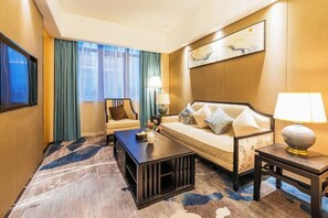A hotel room with a sofa, a coffee table, a TV, and a painting on the wall. - Sovereign Garden Hotel (Cangnan)
