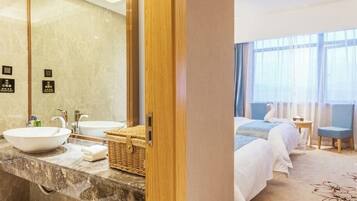 A hotel room with a marble bathroom vanity, two sinks, a large mirror, and a bed with a blue headboard.