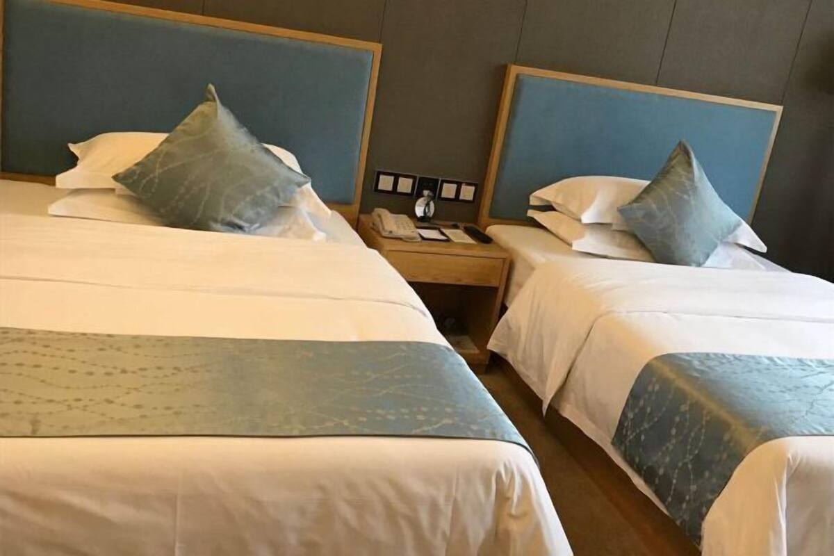 Une chambre d’hôtel avec deux lits, chacun doté d’une tête de lit et d’oreillers. Une table de chevet se trouve entre les lits, avec un téléphone et une petite table.