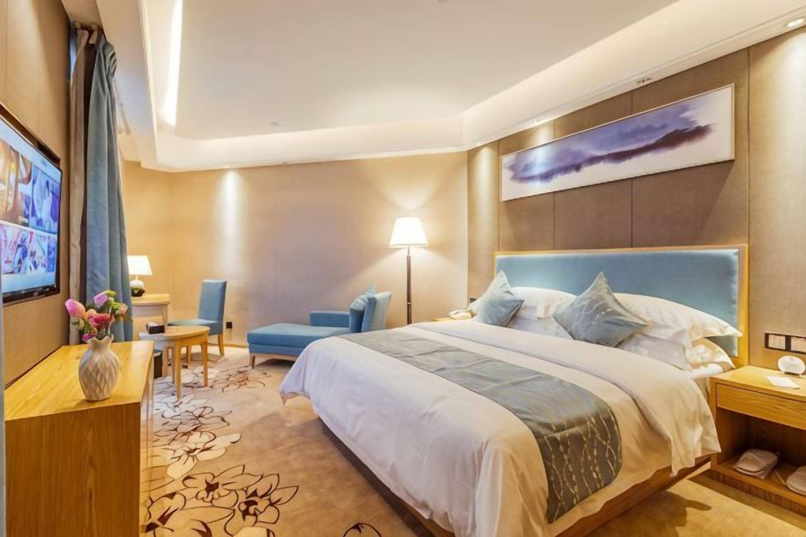 A hotel room with a large bed, a desk, a chair, a TV, and a painting on the wall.