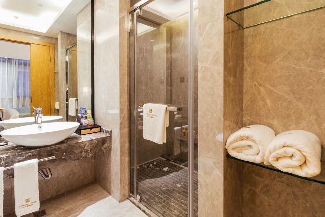 A modern bathroom with a glass shower enclosure, a marble countertop, and a glass shelf with towels.