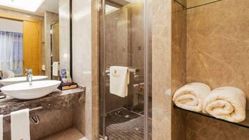 A modern bathroom with a glass shower enclosure, a marble countertop, and a glass shelf with towels.