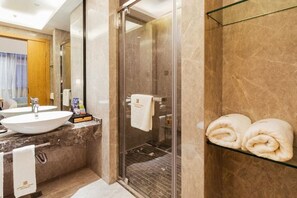 A modern bathroom with a glass shower enclosure, a marble countertop, and a glass shelf with towels. - Sovereign Garden Hotel (Cangnan)