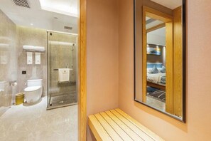 A modern bathroom with a glass shower enclosure, a wooden bench, and a large mirror reflecting a bedroom with a bed and a nightstand. - Sovereign Garden Hotel (Cangnan)