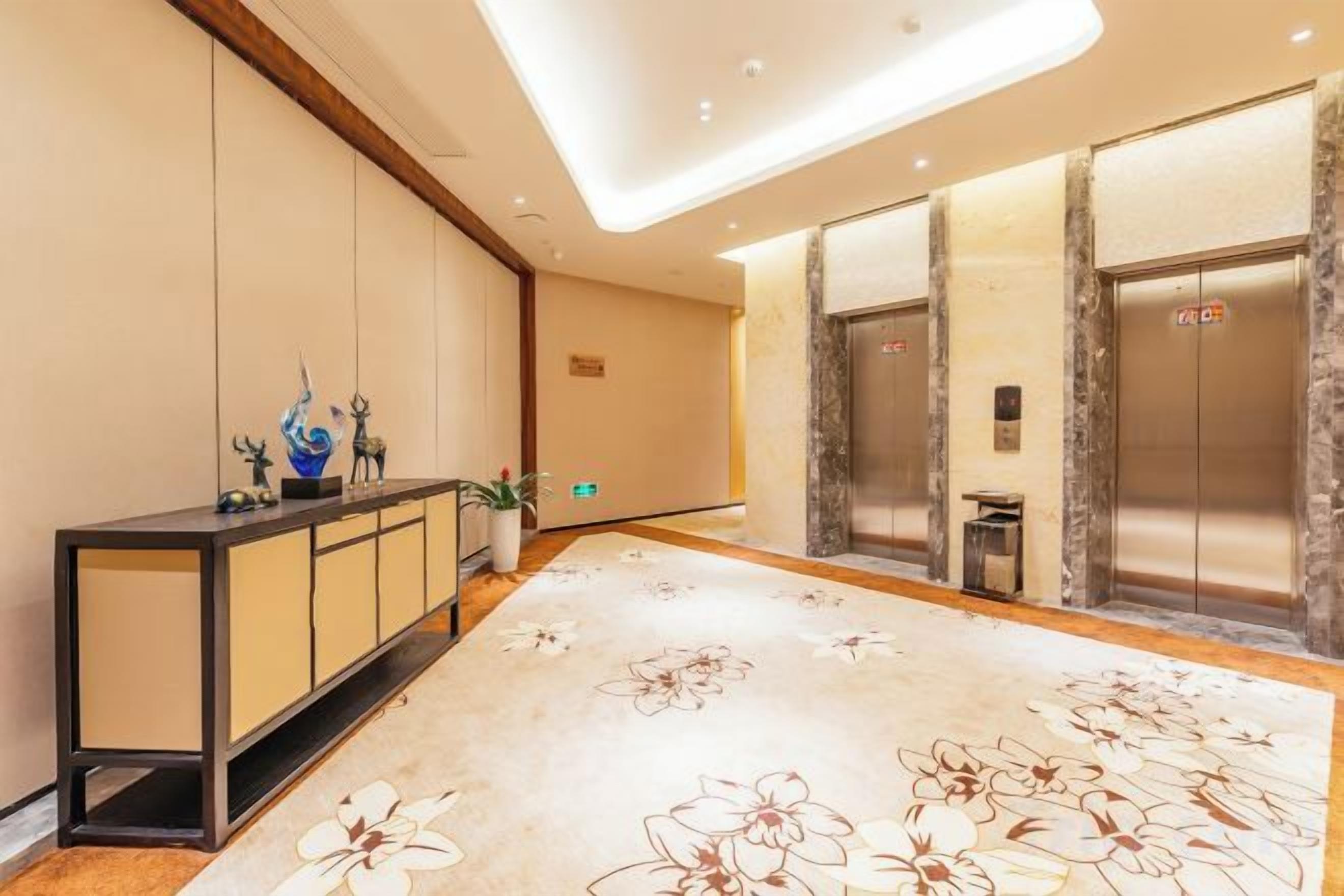 Un vestíbulo de hotel con mostrador de recepción, ascensores y una alfombra estampada.