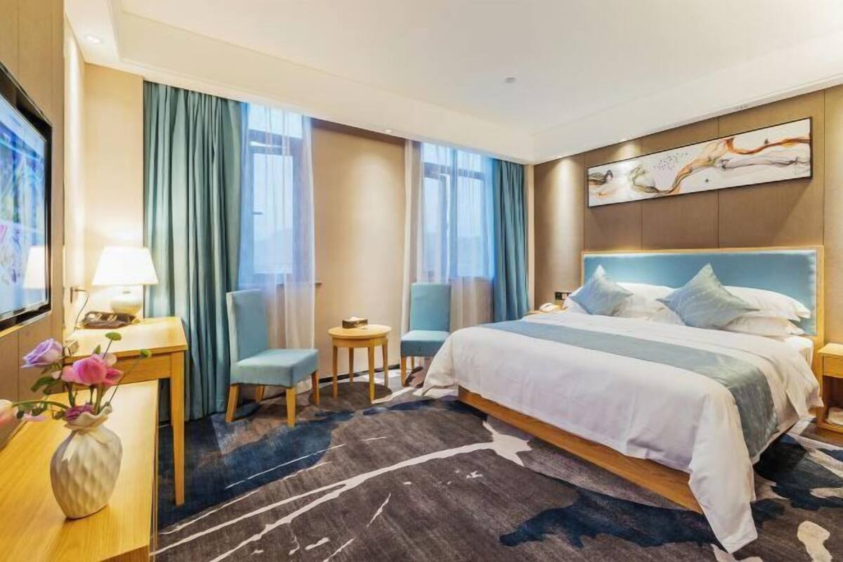 Une chambre d’hôtel avec un grand lit, un bureau avec une lampe, deux chaises et un téléviseur.