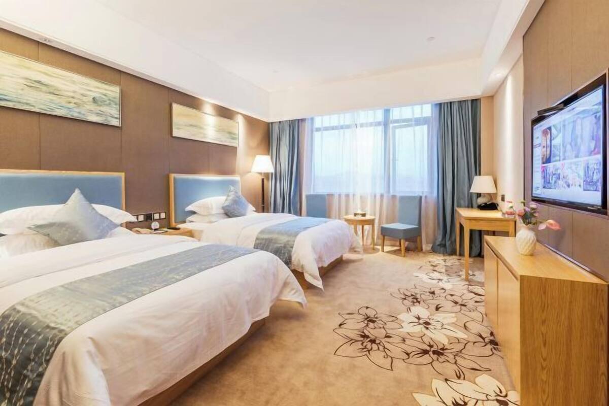 Une chambre d’hôtel avec deux lits, une télévision, un bureau et une fenêtre avec des rideaux.
