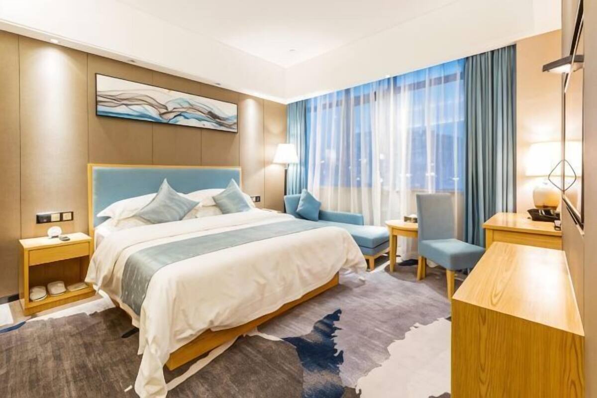 Une chambre d’hôtel avec un lit, un bureau, une chaise, une table de chevet et une fenêtre avec des rideaux.