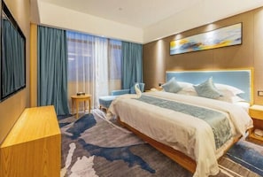 A hotel room with a large bed, a small side table, a chair, and a desk. - Sovereign Garden Hotel (Cangnan)