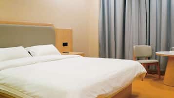 A hotel room with a large bed, a chair, a small table, and curtains.
