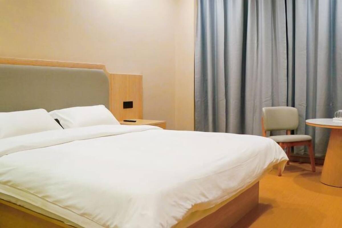 A hotel room with a large bed, a chair, a small table, and a lamp.