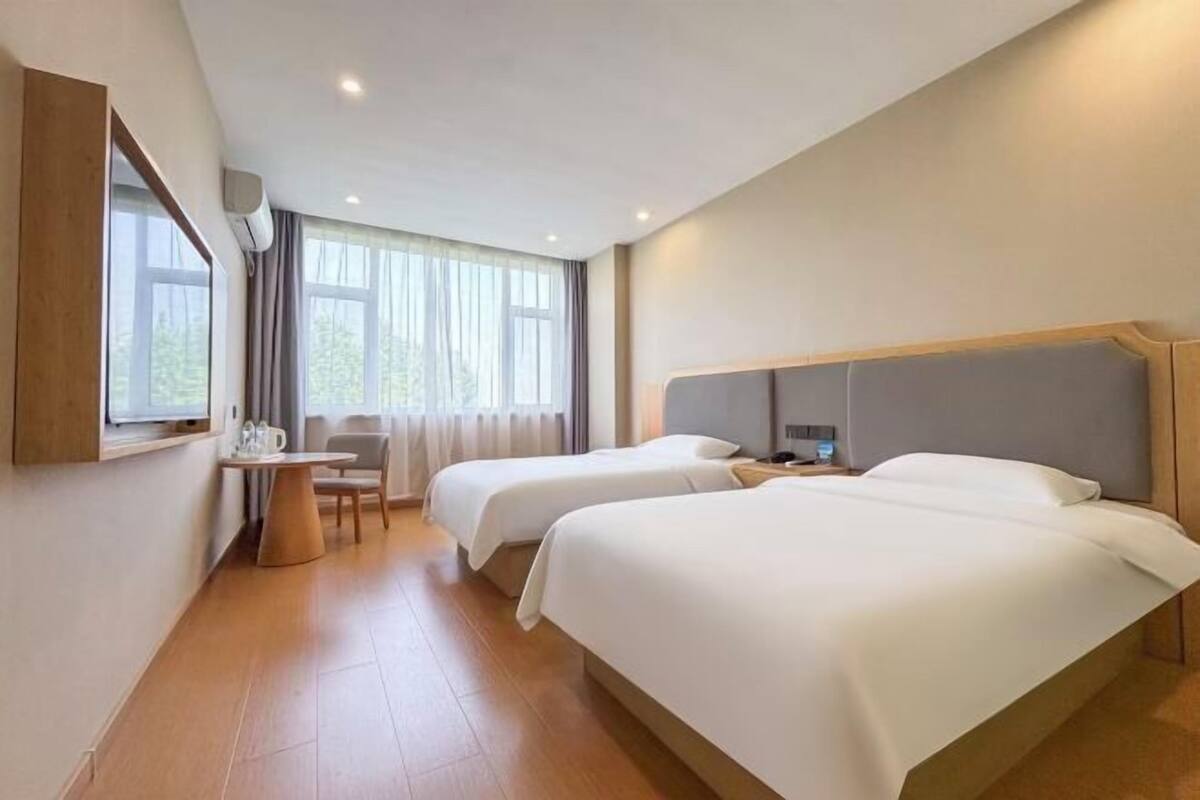 A hotel room with two beds, a desk, a chair, and a window with curtains.
