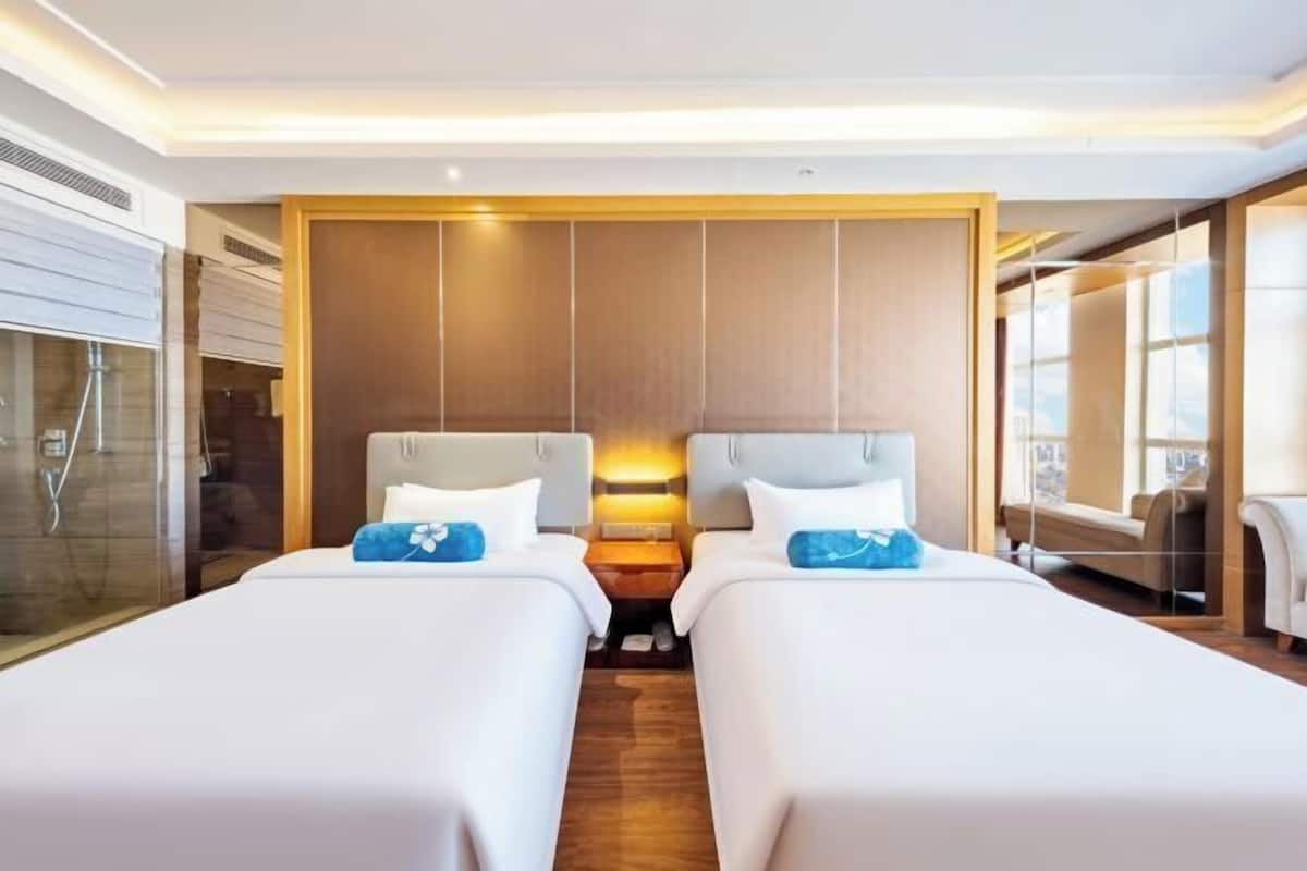 Ein Hotelzimmer mit zwei Betten, einer Wandpaneele aus Holz, einer Duschkabine aus Glas und Blick auf die Stadt.