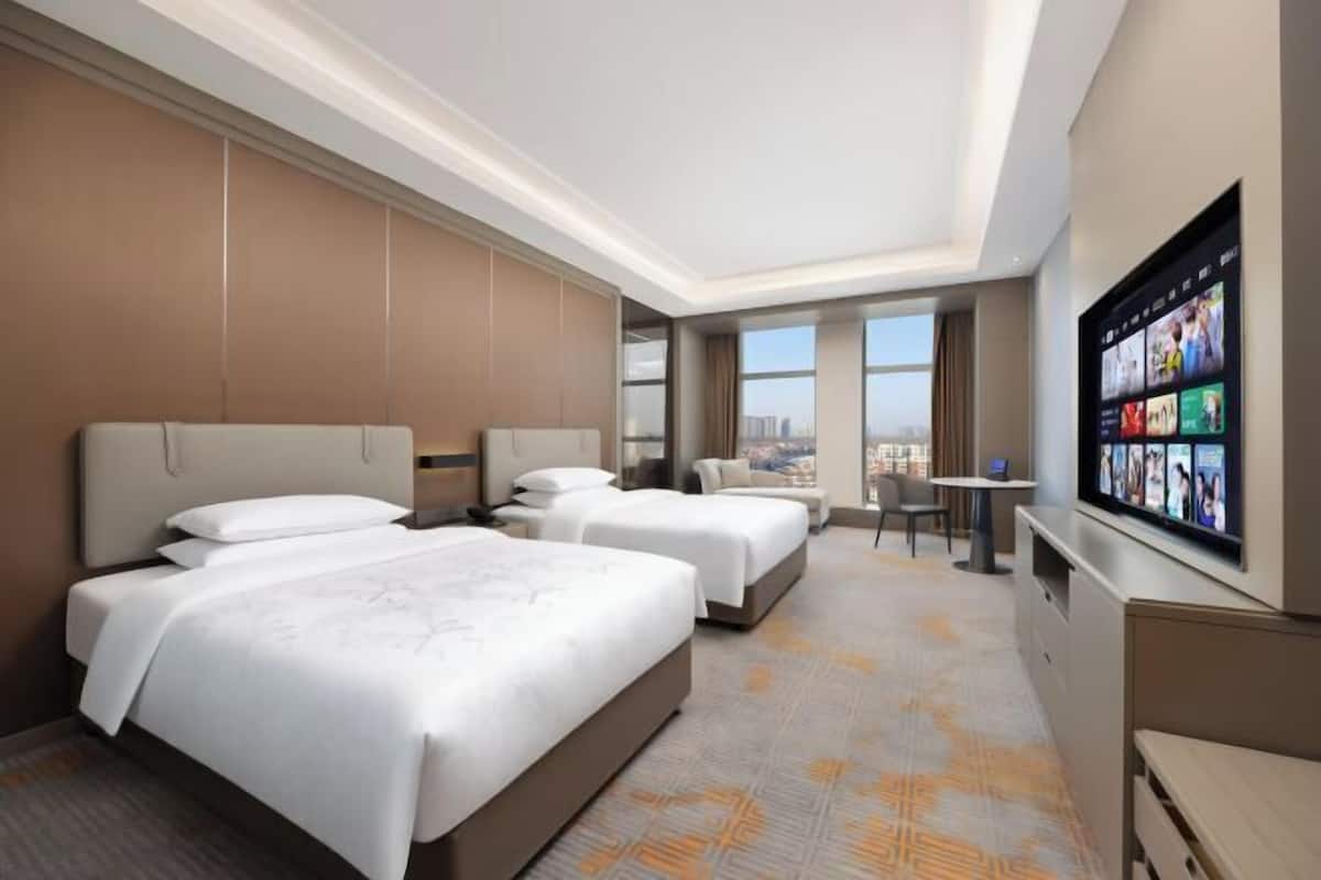 Ein Hotelzimmer mit zwei Betten, einem Fernseher, einem Schreibtisch und Blick auf die Stadt.