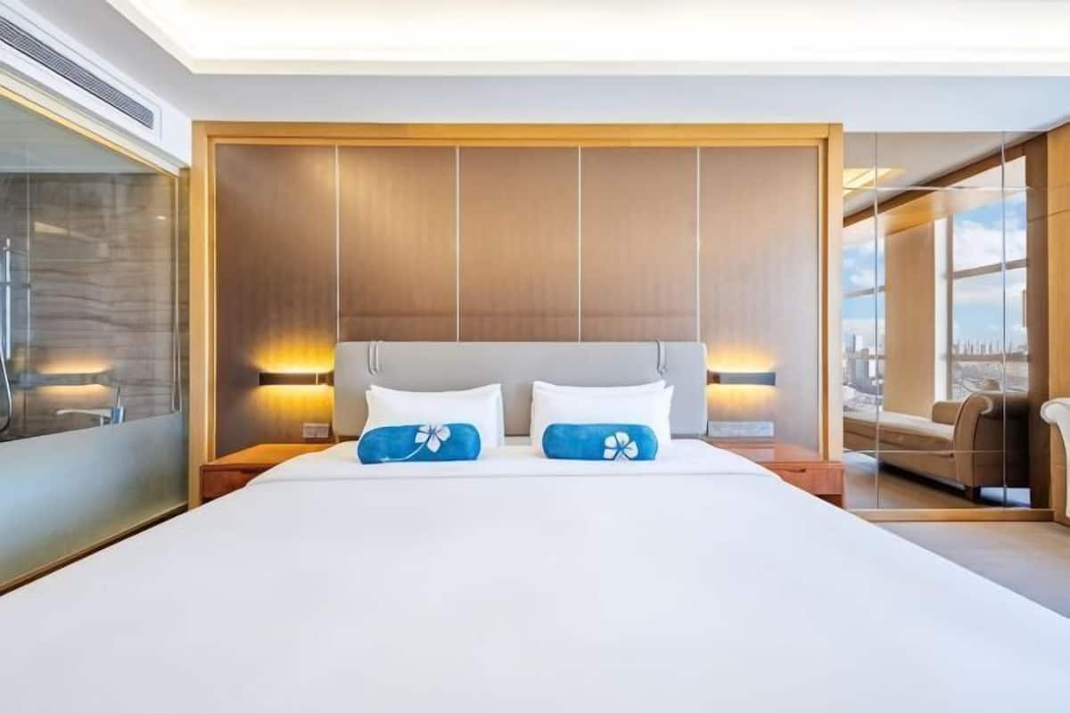 Ein modernes Hotelzimmer mit einem großen Bett, einem Holz-Kopfteil, Nachttischlampen und Blick auf die Stadt.