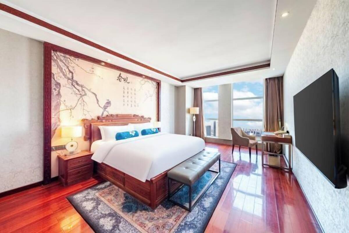 Ein Hotelzimmer mit einem großen Bett, einem Schreibtisch, einem Stuhl, einem Fernseher und einem Fenster mit Blick auf die Stadt.