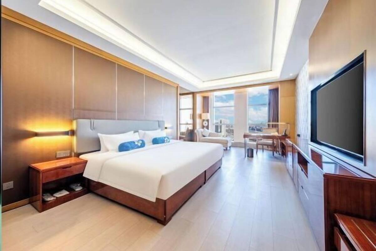 Ein modernes Hotelzimmer mit einem großen Bett, einem Fernseher und einem Balkon mit Blick auf die Stadt.