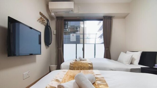 A hotel room with two beds, a flat-screen TV, an air conditioning unit, and a view of the outside. - toho residence (Osaka)
