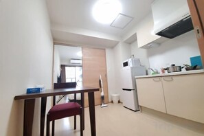 A compact kitchen with a refrigerator, microwave, and stove. There is a dining table with a chair in the foreground. - toho residence (Osaka)