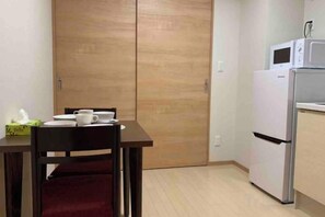 A small kitchenette with a microwave and refrigerator, a dining table with chairs, and a sliding door. - toho residence (Osaka)