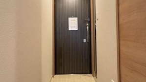 A narrow hallway with a dark wooden door, a light switch, and a small sign on the door. - toho residence (Osaka)