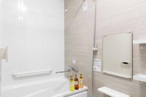 Une salle de bain avec une baignoire, une douche et un miroir au mur.