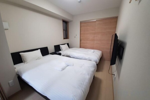Une chambre d’hôtel avec deux lits, une porte en bois et un téléviseur fixé au mur.