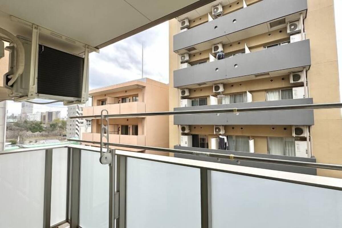 Un immeuble résidentiel à plusieurs étages, doté de balcons, de climatiseurs et offrant une vue sur le paysage urbain.