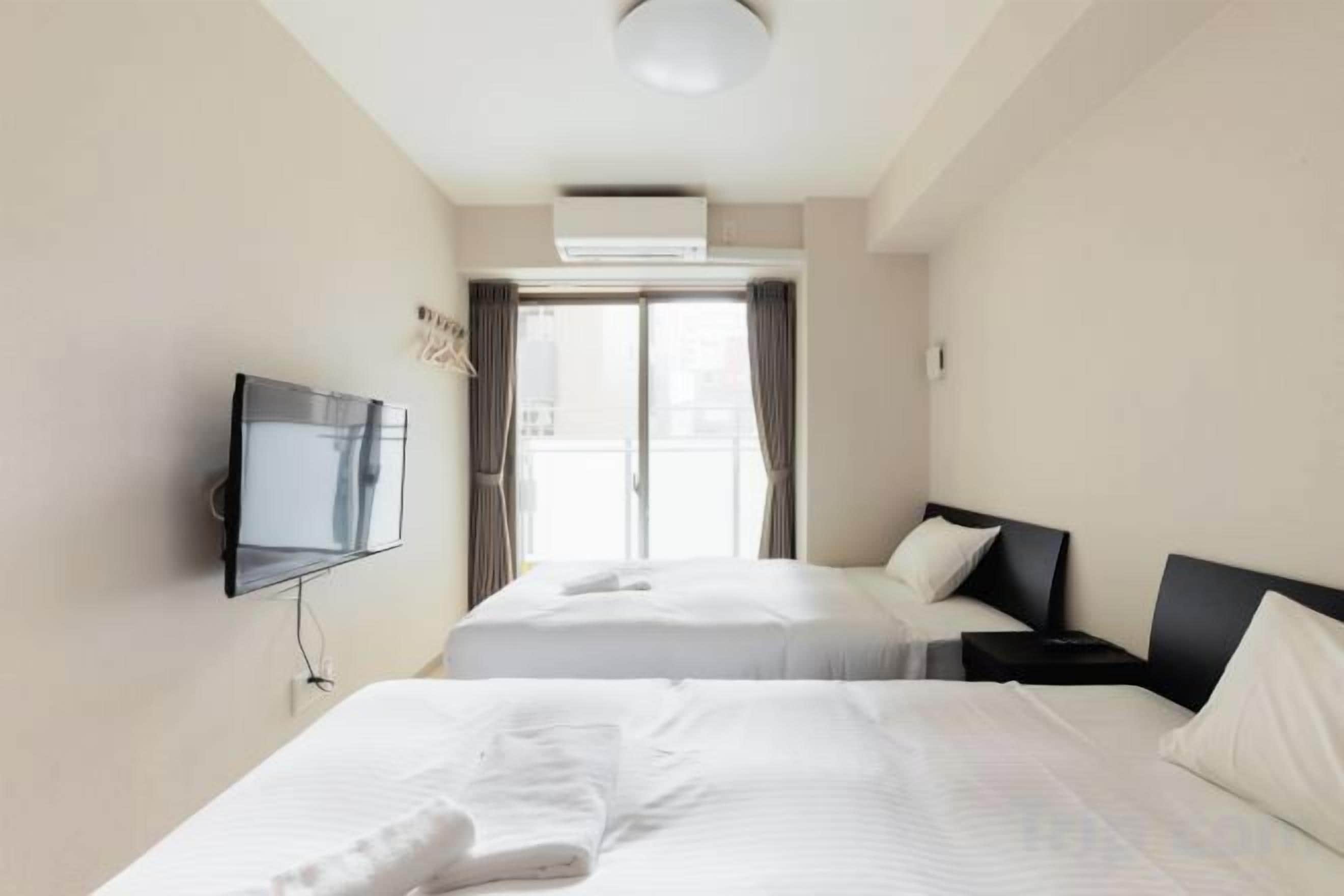 A hotel room with two beds, a TV, and a view of the outdoors.