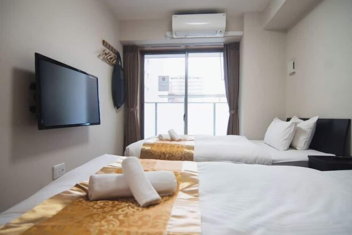 Une chambre d’hôtel avec deux lits, un téléviseur à écran plat, un appareil de climatisation et une fenêtre avec des rideaux.