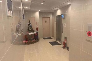Un pasillo con un árbol de Navidad y regalos, un ascensor y un detector de incendios.