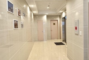 A corridor with a tiled floor, doors, and a wall-mounted intercom. - toho residence (Osaka)