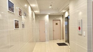 A modern hallway with a tiled floor, a series of doors, and a security intercom on the wall. - toho residence (Osaka)