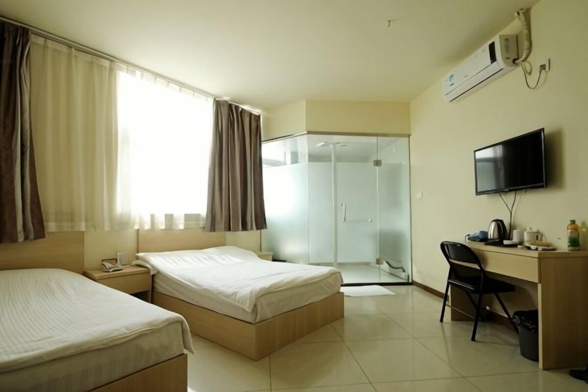 A hotel room with two beds, a desk with a chair, a television, and a walk-in closet.