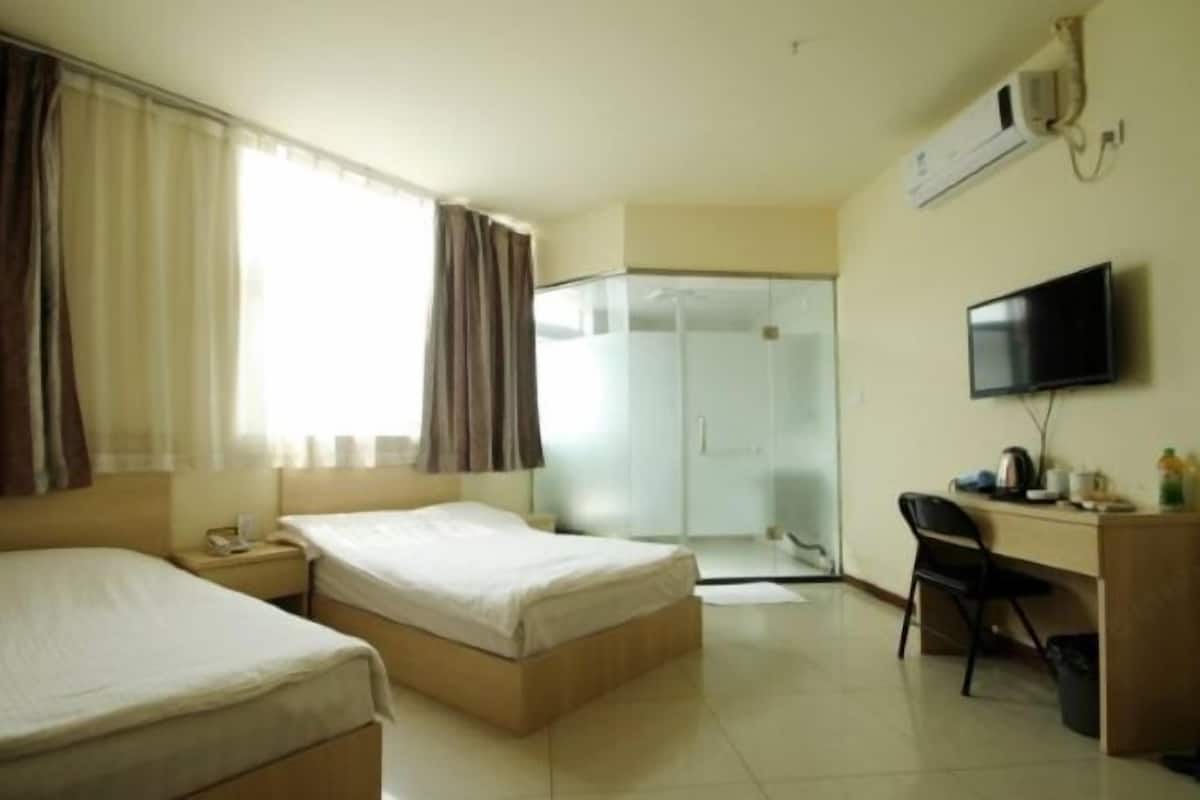 A hotel room with two beds, a desk, a chair, a TV, and a shower area.