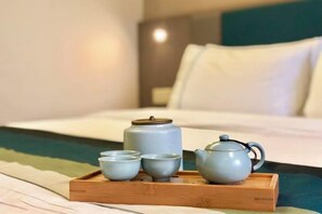 Una bandeja con tetera y tazas sobre una cama con almohada y cabecera.