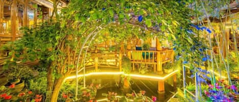 An indoor garden with a wooden bridge, a pond, and lush greenery.