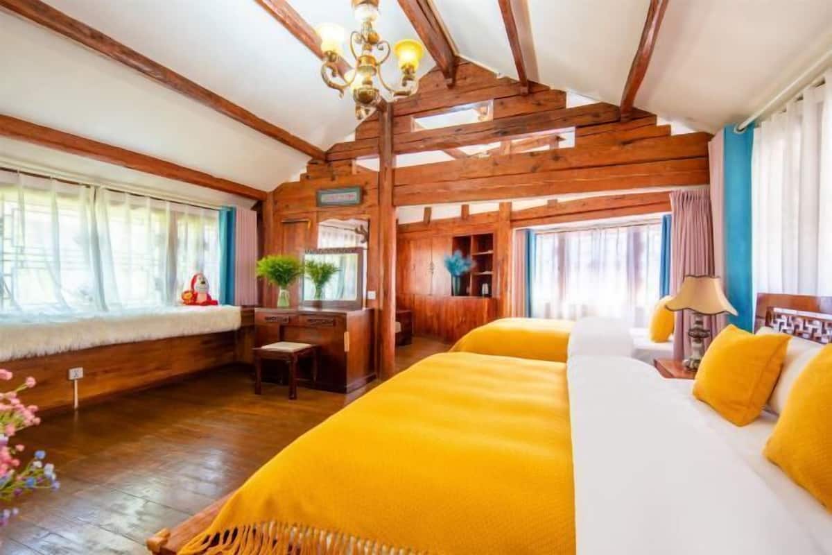 A room with wooden beams, a bed with yellow bedding, a desk with a lamp, and a window with curtains.