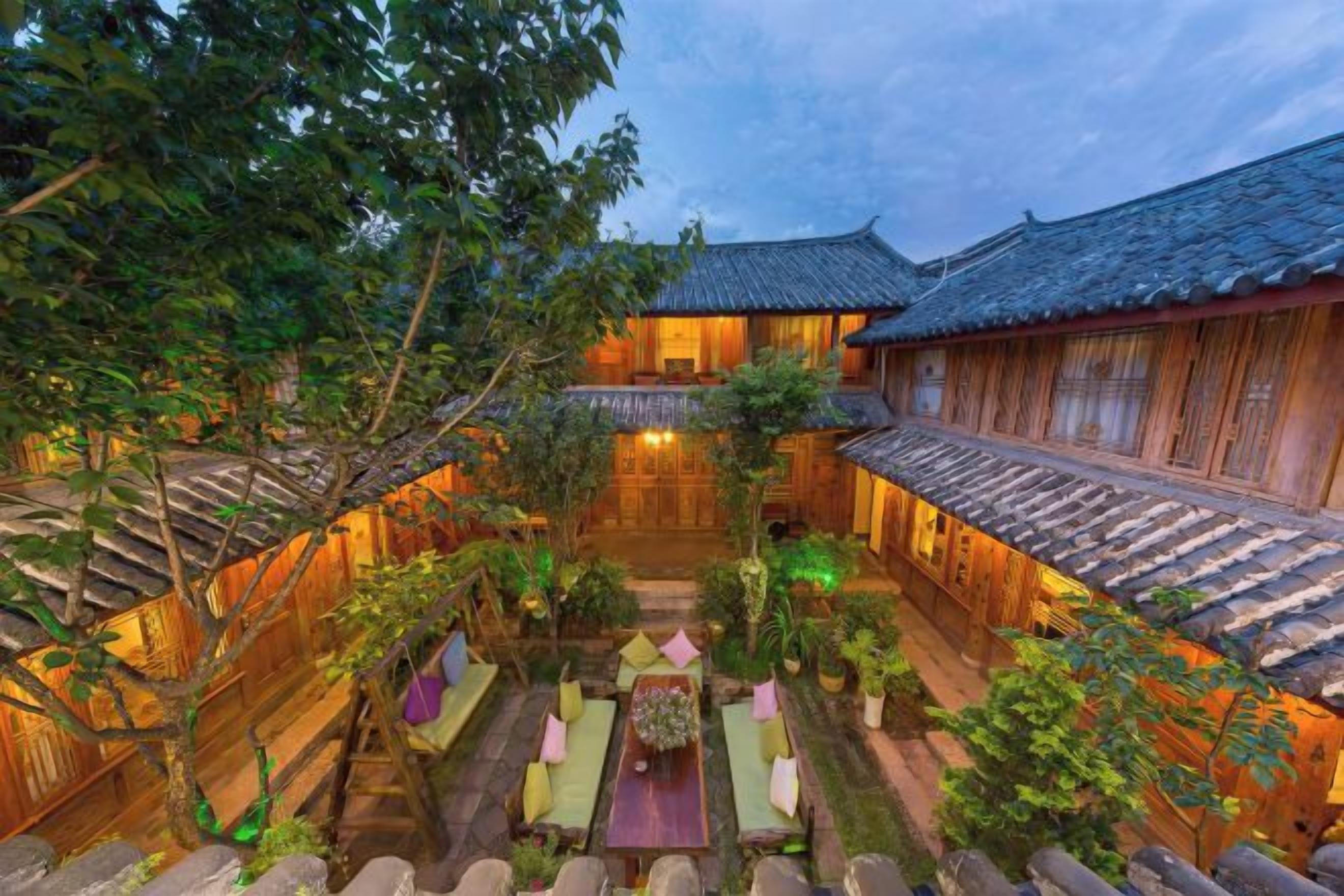 A traditional courtyard with wooden buildings, a central seating area, and a stone pathway.