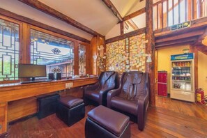 Una habitación con techo de madera, un televisor sobre un escritorio, dos sillones de cuero, un refrigerador pequeño y una pared cubierta de notas.