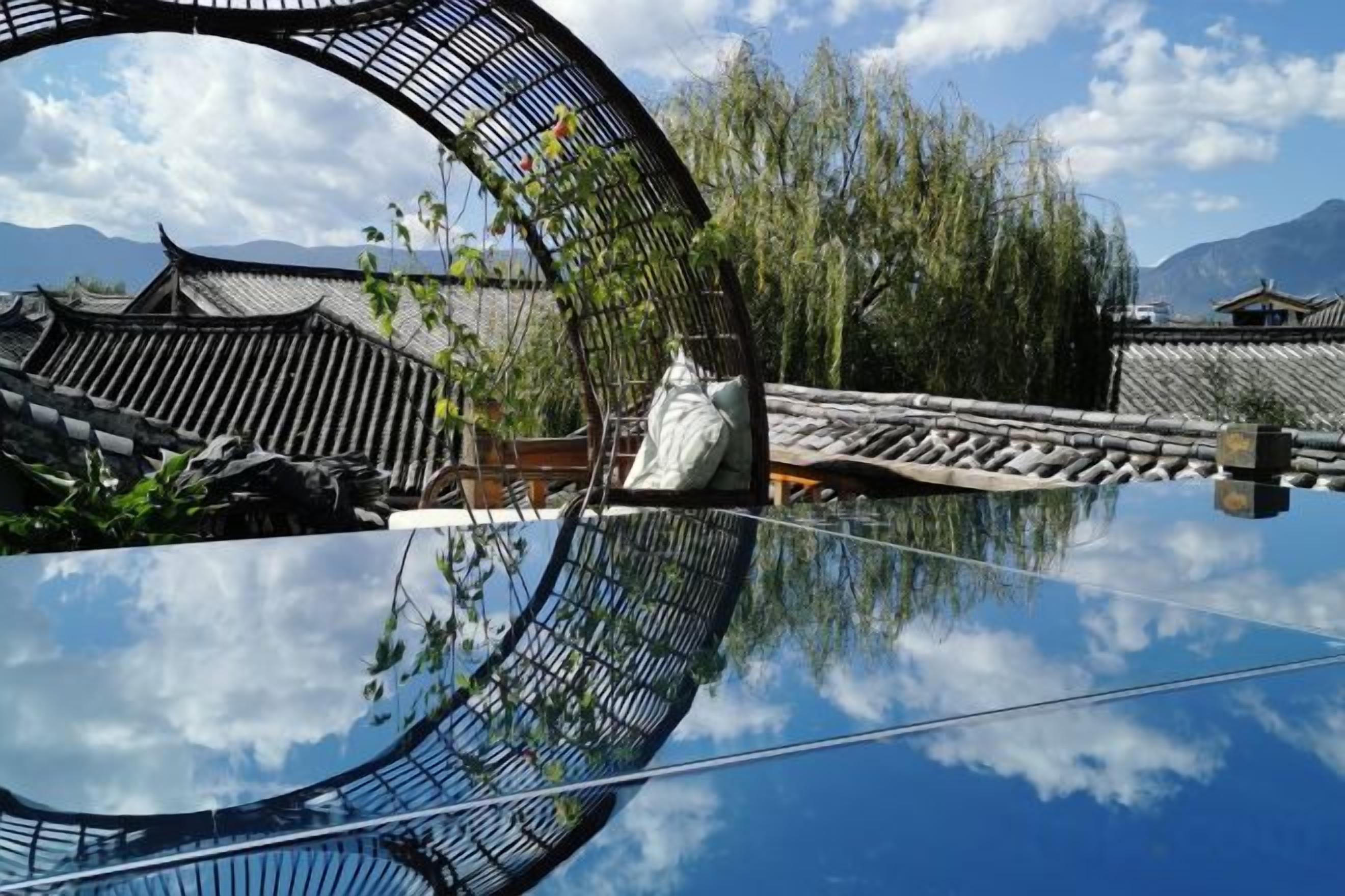 Pátio chinês tradicional com reflexo nítido na água, cercado por edifícios com telhados de cerâmica.