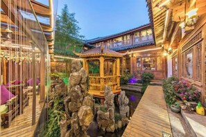 A traditional Chinese courtyard with a wooden pavilion, a koi pond, and a wooden walkway. - Xin Zhoujia Courtyard (Lijiang)
