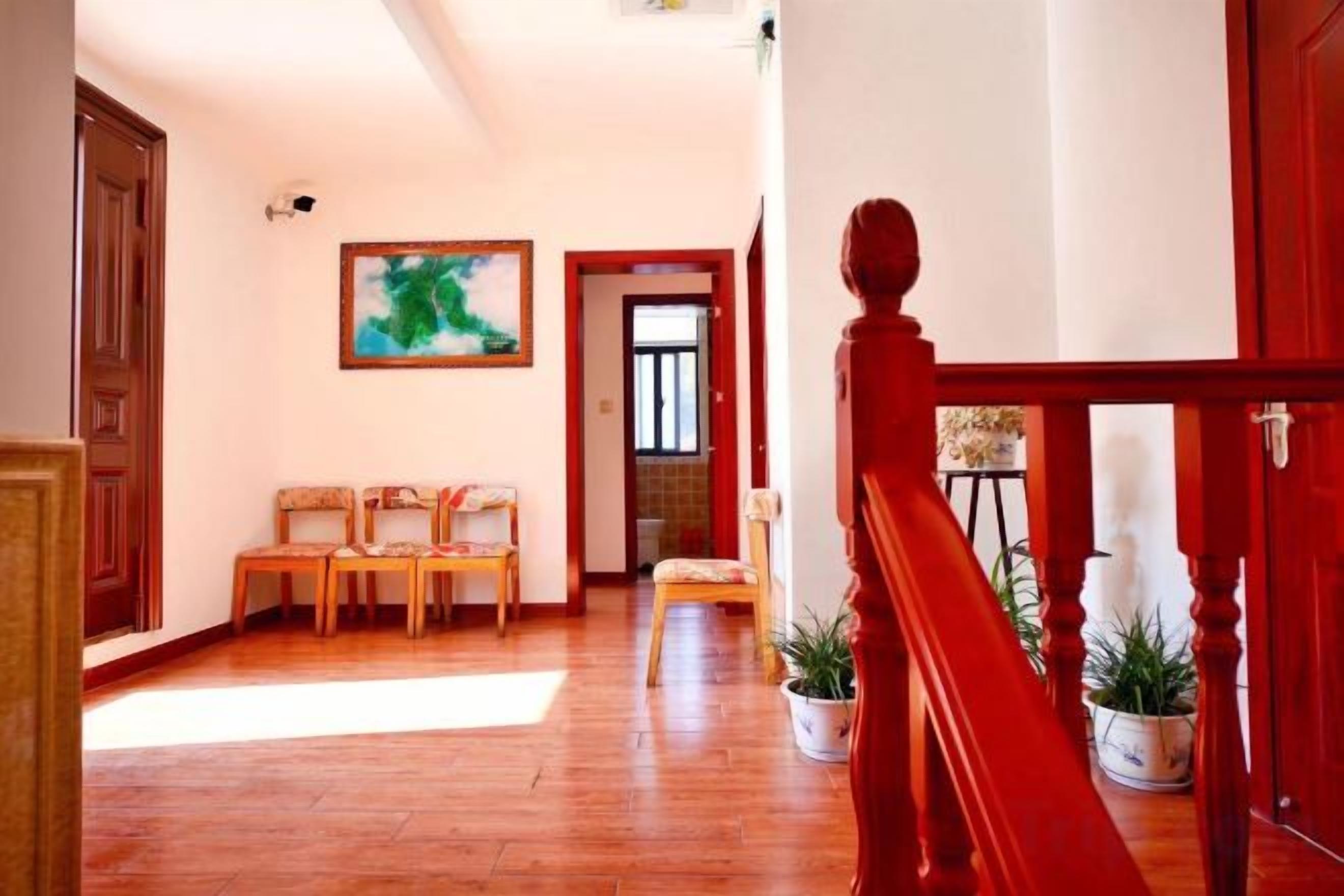 A hallway with wooden flooring, a red staircase, and a seating area with chairs.