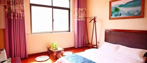 A room with a bed, a window, a painting, and a small table with a plant.