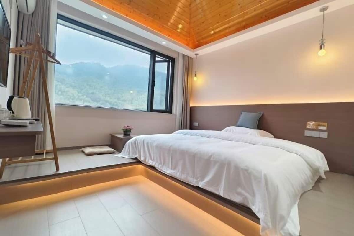 Une chambre moderne avec un grand lit, un plafond en bois, une vue sur les montagnes et une table de chevet avec une lampe.
