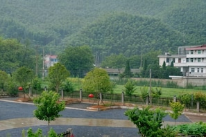 A residential area with a paved driveway, a fenced garden, and a backdrop of a hilly landscape. - Ningguo Travellers Homestay (Ningguo)