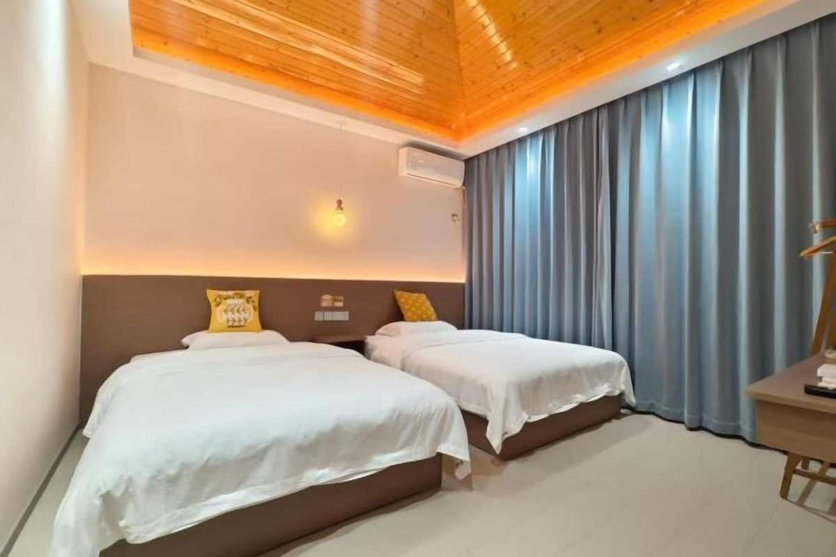 Une chambre d’hôtel avec deux lits, un plafond en bois, un rideau gris et un bureau avec une lampe.