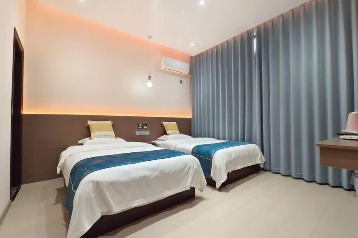 Une chambre d’hôtel avec deux lits, un bureau et une grande fenêtre avec des rideaux.