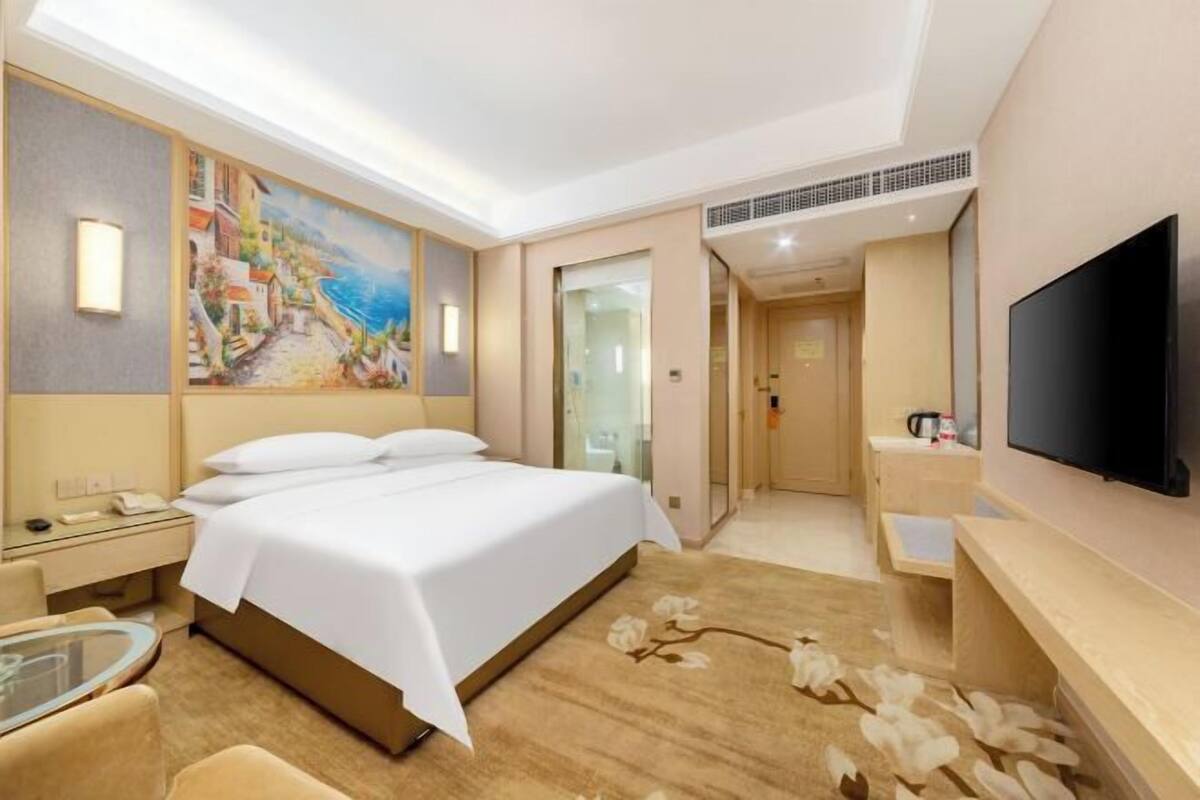 A hotel room with a bed, bedside table, TV, and a painting on the wall.